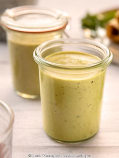 two jars filled with green sauce sitting on top of a table next to other dishes