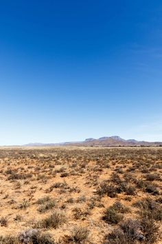 an empty field in the middle of nowhere, with mountains in the distance and blue sky