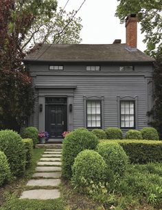 a gray house surrounded by hedges and trees