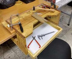 a wooden workbench with scissors and pliers in the bottom drawer, on top of a desk