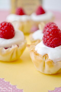 small cupcakes with white frosting and raspberries on top are sitting on a plate