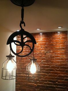 two light fixtures hanging from the ceiling in front of a brick wall with lights on it