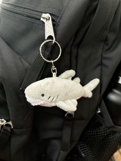 a stuffed shark is in the pocket of a black backpack with a keychain