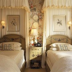 two twin beds in a bedroom with floral wallpaper and white drapes on the windows