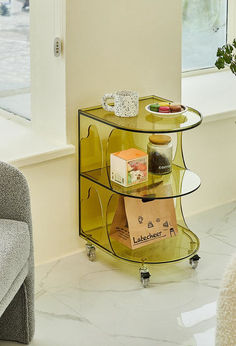 a glass shelf with various items on it next to a chair and window in a living room