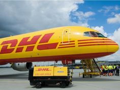 a dhl airplane parked on the tarmac at an airport with people standing around it