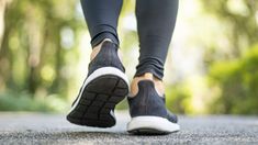 a woman's feet in black and white shoes walking down the street with trees in the background