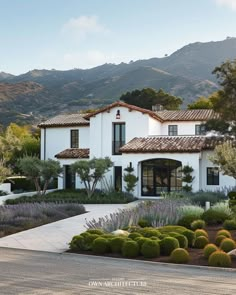 a large white house with lots of bushes and trees around it's front entrance