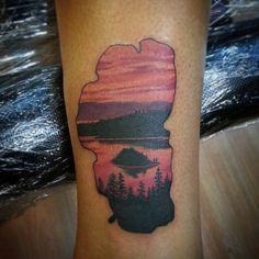 a tattoo on the leg of a person with a lake and mountains in the background