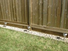 the side of a wooden fence with two lights on it and grass in front of it