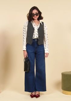 a woman standing in front of a beige wall wearing blue jeans and a white shirt