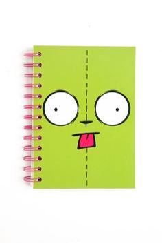 a green notebook with a face drawn on it and pink pencils next to it