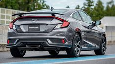 the rear end of a gray honda civic hatchback driving on a road with trees in the background