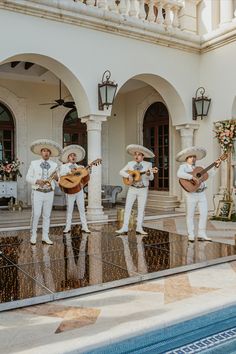 three men in white outfits are playing guitars near a swimming pool and some flowers on the ledge