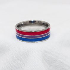 a silver ring with red, blue and purple stripes on it sitting on a white cloth