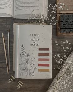 an open book sitting on top of a wooden table next to flowers and pencils