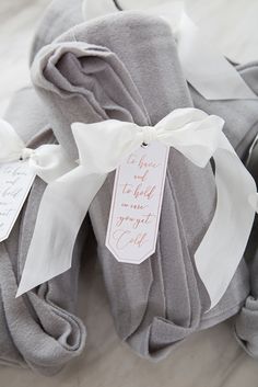 two gray blankets with white ribbons tied around them and tags attached to the top one