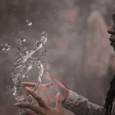 a woman holding her hands out to the water in front of her face and looking at it