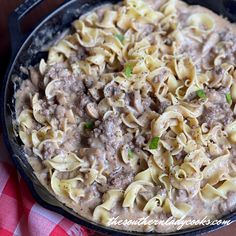 a skillet filled with pasta and meat sauce on top of a checkered table cloth