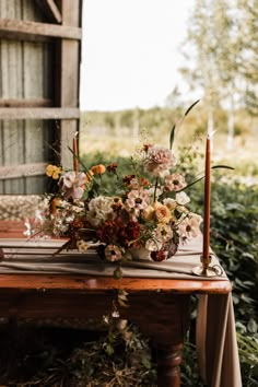 a wooden table topped with a vase filled with flowers next to a tall candle holder