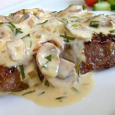 a steak covered in mushrooms and sauce on a white plate next to a side of veggies