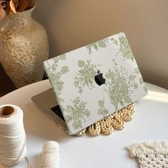 an apple laptop sitting on top of a table next to yarn and spools of thread