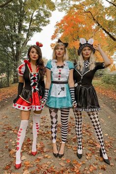 three women dressed in costumes posing for the camera on a dirt road with leaves all around them