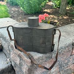 an old fashioned camera bag sitting on top of a stone wall with flowers in the background