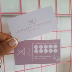 a person holding up a business card in front of a pink netted wall with flowers on it