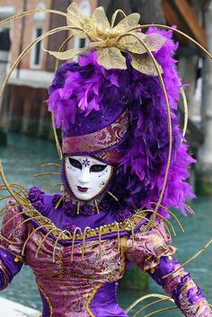 a woman in a purple and gold costume with feathers on her head, wearing a mask