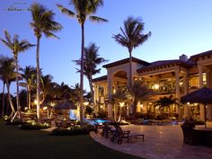 a large house with palm trees and lawn chairs in front of it at night time