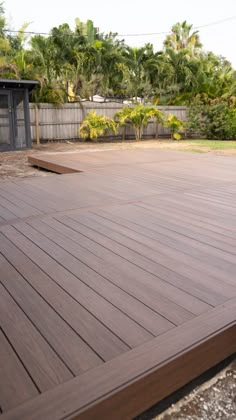 a large wooden deck in the middle of a yard with trees and bushes behind it