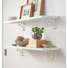 two white shelves with pots and bowls on them, one has a potted plant