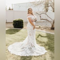 a woman in a wedding dress standing on the grass with her arms around her waist