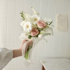 a woman holding a bouquet of white and pink flowers in her left hand while standing next to a counter