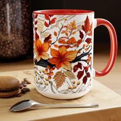 a red and white coffee mug sitting on top of a wooden table next to a spoon