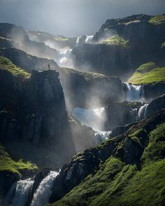 a man standing on the edge of a waterfall surrounded by lush green hills and grass