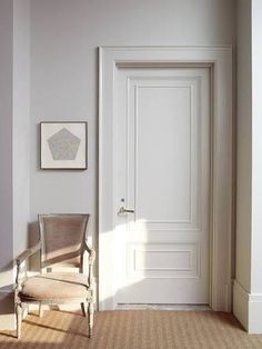 an empty chair in front of a door with a painting on the wall next to it