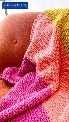 a knitted blanket sitting on top of a couch next to a pink and yellow pillow