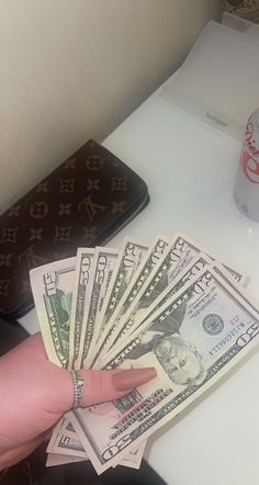 a person's hand holding money in front of a purse