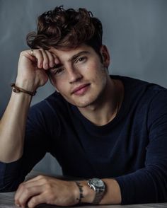 a young man sitting at a table with his hand on his head and looking off to the side