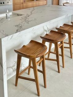 four wooden stools sit at the edge of a marble countertop in a kitchen