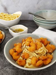 a bowl filled with pasta and shrimp on top of a table next to bowls of sauce