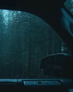 the inside of a car with rain drops on the windshield and trees in the background