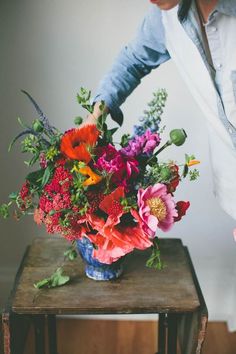 a woman arranging flowers in a blue vase on a small table with an instagram page