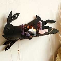 a shelf with candles, rocks and other items hanging from it's sides on the wall