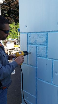 a man using a power drill to paint a brick wall with blue foam on it