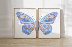 two blue and gold butterfly paintings on white walls in an empty room with wood flooring