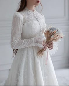 a woman in a white dress holding flowers and wearing a tiara with long sleeves