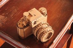 a camera made out of cardboard sitting on top of a wooden table next to a cup